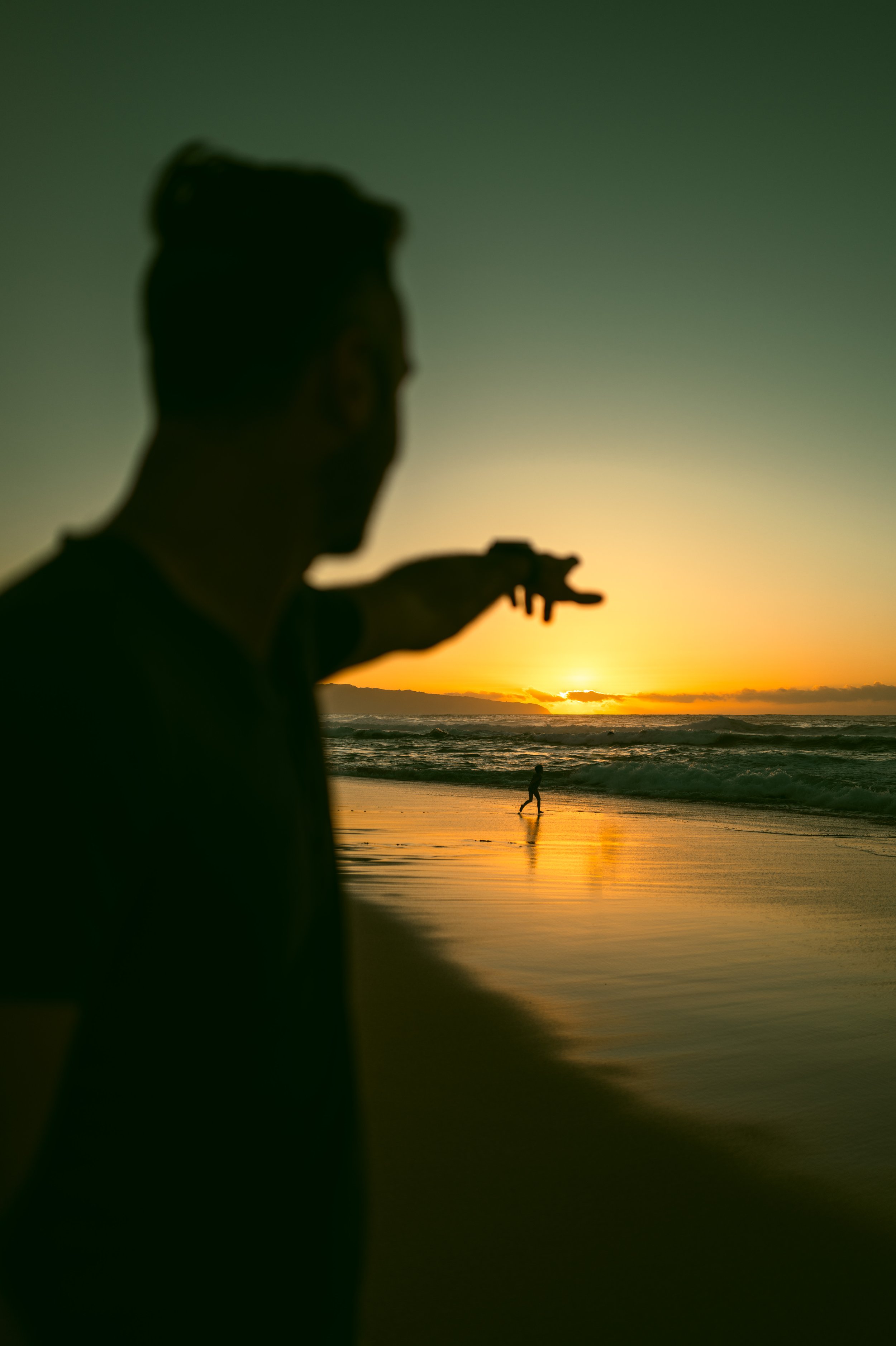 Silhouette of a person reaching toward the horizon at a golden Hawaiian beach sunset